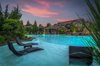 A pool with lounge chairs and a house in the background during sunset.